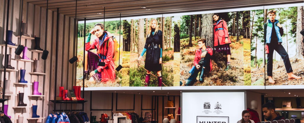 Hunter store interior with models wearing rain gear against a forest backdrop and colorful boots on display.