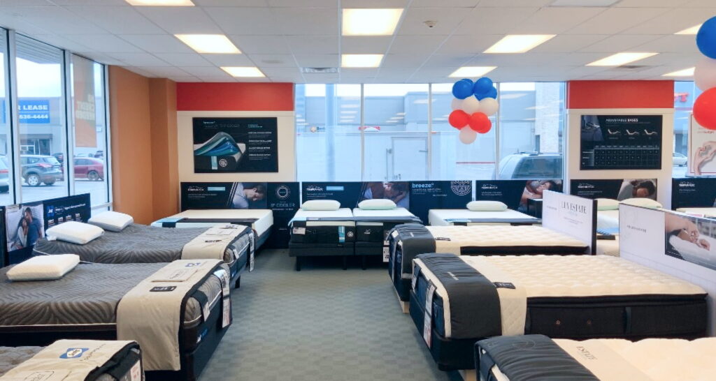 A brightly lit mattress store showroom showcasing various beds, informational displays, and festive balloons.