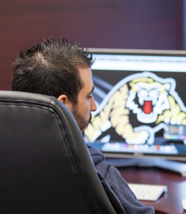 A man looks at a computer monitor displaying a tiger logo.