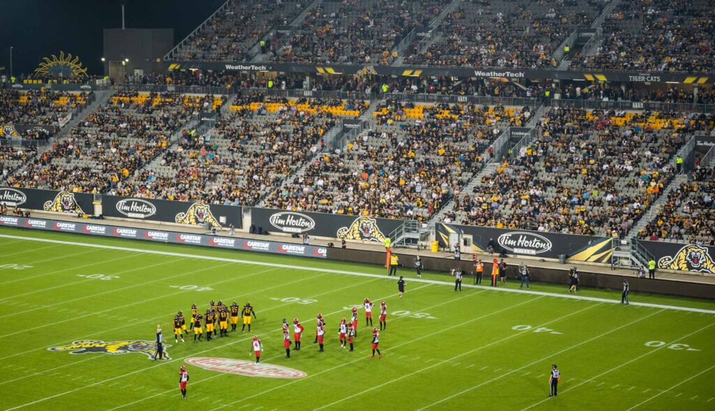 A night football game in a brightly lit stadium, with players on the field and spectators in the stands.