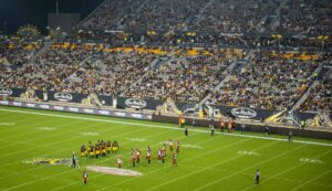 A night football game in a brightly lit stadium, with players on the field and spectators in the stands.