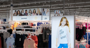 A brightly lit Walmart clothing department filled with racks of women's and girls' apparel under overhead signs featuring models.