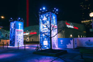 Brightly lit blue and white banners for the Nissan Titan Street Festival and Grey Cup Festival stand at night in front of Ripley's Aquarium of Canada and a red tower.