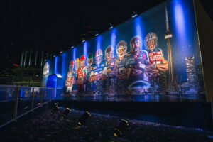 "An outdoor night display shows Canadian football players superimposed on the Toronto skyline, advertising the 2016 Grey Cup."