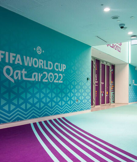 "An empty, brightly lit hallway features vibrant turquoise walls with ""FIFA World Cup Qatar 2022"" branding and a light blue and purple patterned floor."