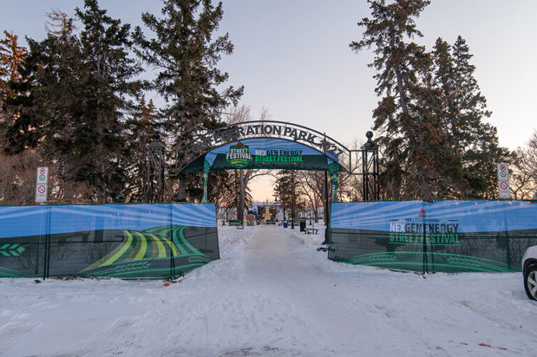 "A snow-covered pathway leads through the archway of Confederation Park, adorned with banners for the NexGen Energy Street Festival."
