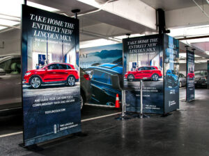 An automotive event in a parking garage features multiple large banners promoting overnight test drives for red and blue Lincoln MKX SUVs.