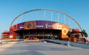 A large stadium featuring FIFA World Cup Qatar 2022 branding and a prominent arch structure under a clear blue sky.