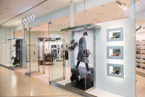 "A modern Ecco shoe store with a glass exterior, displaying shoes and promotional imagery."