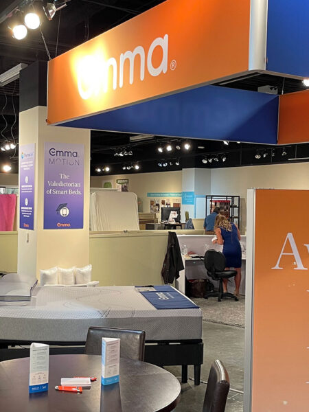 An Emma mattress showroom featuring branded displays, multiple beds, and customers browsing.