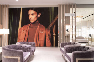 "Interior of a Jimmy Choo boutique featuring a large display of a woman in an orange coat, with plush purple armchairs in the foreground."