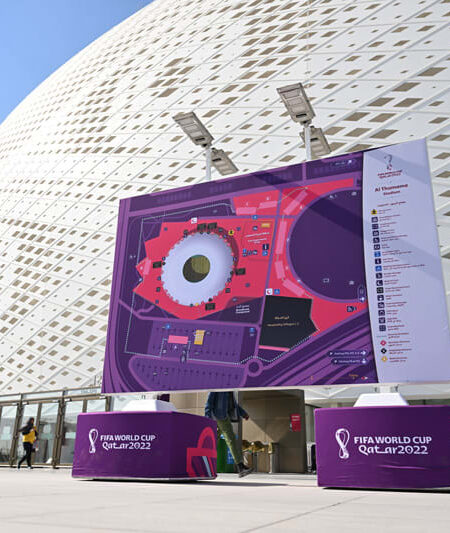 "The exterior of Al Thumama Stadium, a white patterned building, with a large map and FIFA World Cup Qatar 2022 branding in the foreground."