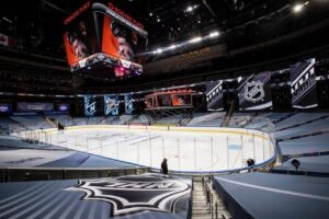 "An empty Rogers Place NHL arena set up for the Stanley Cup Qualifiers, with a large jumbotron over the ice and prominent NHL branding throughout."