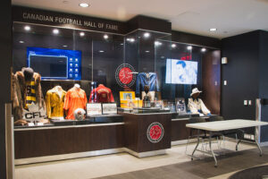 "The Canadian Football Hall of Fame features display cases filled with historic jerseys, helmets, trophies, and interactive screens."