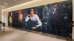"A large wall mural in a retail store displays diverse fashion models in stylish clothing against a snowy, festive forest backdrop."