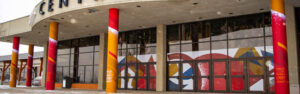 Colorful building entrance with pillars wrapped in red and orange graphics and windows featuring abstract geometric designs.
