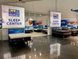A Rooms To Go Outlet Sleep Center showroom displays multiple mattresses with large promotional banners featuring people sleeping.