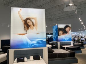 A bright mattress showroom showcases multiple beds and large advertisements of smiling people in bed.