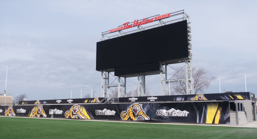 Tim Hortons Field with a large scoreboard and yellow and black tiger-logo banners around the playing field.