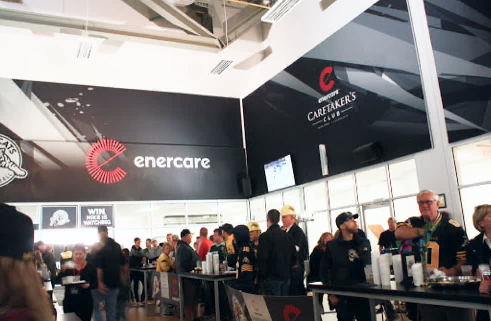 A busy lounge area with many people mingling, featuring large black walls branded with ""enercare"" and ""Caretaker's Club.""
