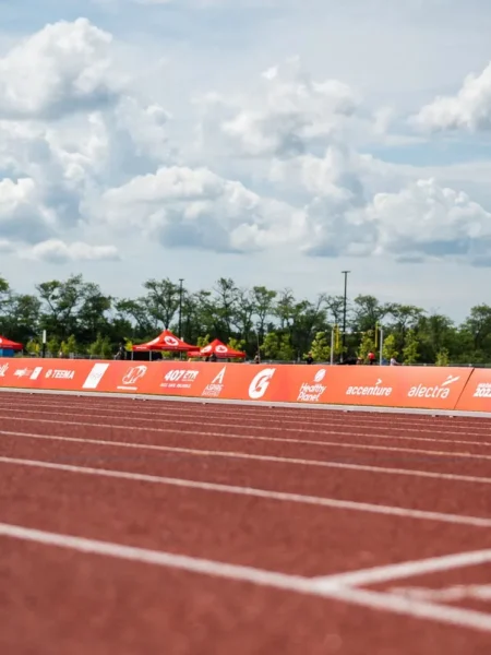 A low-angle view of a red running track alongside an orange banner advertising the Niagara 2022 Canada Games under a cloudy sky.
