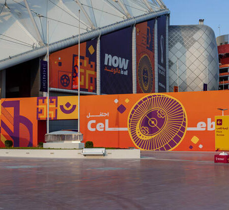 A modern stadium and surrounding buildings are vibrantly decorated with orange and purple FIFA World Cup Qatar 2022 branding.