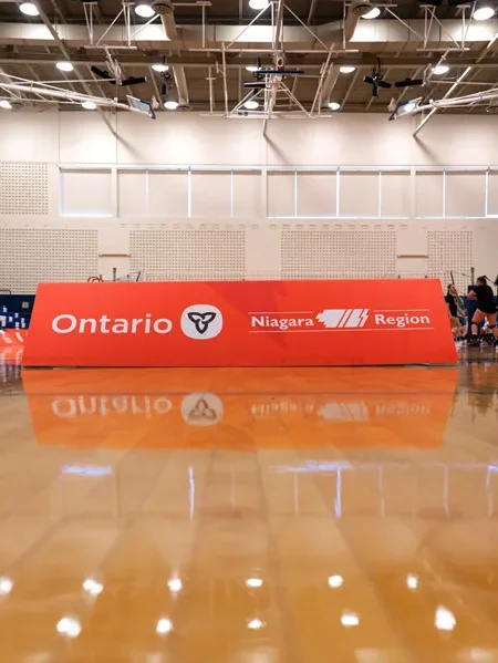 A group of athletes stands behind ""Ontario"" and ""Niagara Region"" banners on a reflective wooden gymnasium floor.
