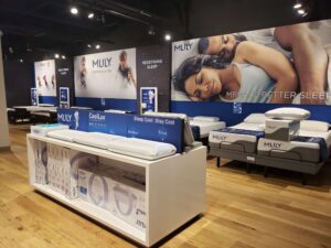 "Interior view of a modern MLILY bedding showroom displaying mattresses, pillows, and branded promotional posters."