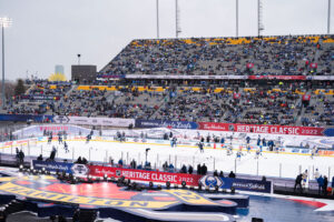 "The Toronto Maple Leafs and Buffalo Sabres play an outdoor hockey game at the Tim Hortons Heritage Classic 2022 in Hamilton, with a large crowd filling the stadium stands."