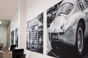 Large black and white prints of a Land Rover and a vintage silver sports car are displayed on an office wall.