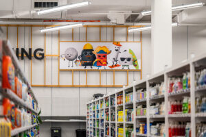 "A store aisle lined with shelves of various products, with a large wall banner depicting five cartoon characters in the background."