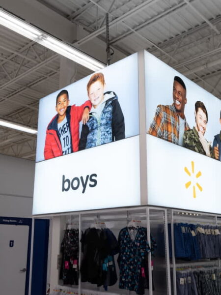 Overhead lighted signs in a Walmart store label clothing sections for 'boys,' 'men,' and 'girls,' featuring images of diverse models.