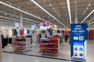 "An interior view of a bright Walmart clothing section with racks and shelves of apparel, alongside a sign promoting online shopping via a QR code."