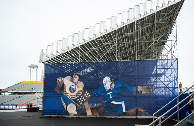 Temporary stadium bleachers with a large banner depicting stylized hockey players from the Buffalo Sabres and Toronto Maple Leafs.