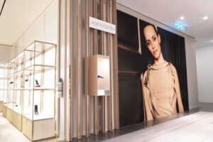An Aquazzura luxury shoe store interior with illuminated displays of footwear and a large poster of a fashion model.