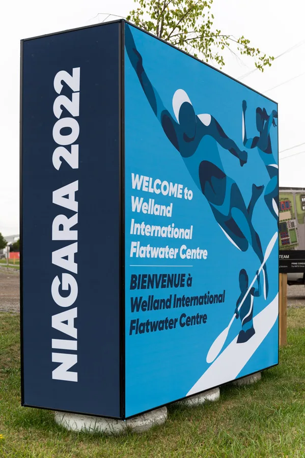 A bilingual sign for Niagara 2022 welcomes visitors to the Welland International Flatwater Centre with water sports graphics.