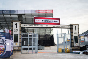 "An exterior view of Gate 1 at an outdoor stadium, featuring large ""Tim Hortons NHL Heritage Classic"" banners overhead."