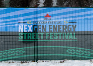 "A mesh banner advertising the ""2022 Grey Cup Festival: NexGen Energy Street Festival"" is displayed over a fence with snow on the ground."