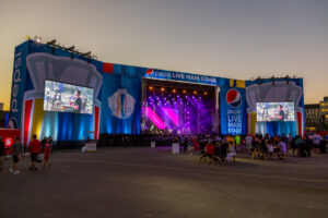 "A large Pepsi Live Main Stage for the 2016 World Cup of Hockey event, with a band performing under purple lights and on prominent side screens, surrounded by attendees."
