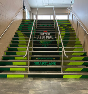 "A staircase decorated in shades of green features ""Grey Cup Festival Saskatchewan"" and ""Bring It To The Heartland"" text on its risers."