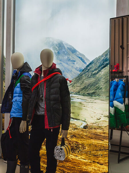 "A retail store displaying winter outdoor apparel on mannequins, racks, and shelves, with a mountain landscape backdrop."