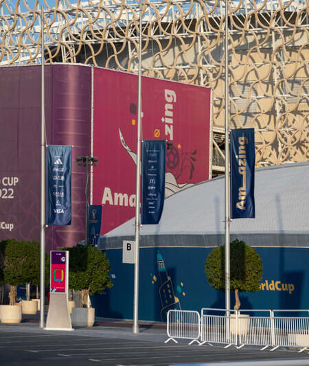 A modern building exterior is decorated with large FIFA World Cup Qatar 2022 banners and promotional flags.