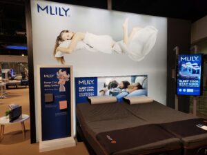 MLILY sleep system showroom display featuring a large banner of a person floating on a mattress and two adjustable beds.