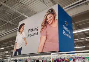 A large overhead Walmart fitting rooms sign featuring a young boy and a smiling woman.