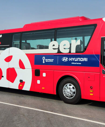 "A red and white bus for the Canadian team, decorated with a soccer ball graphic, ""Cheer!"", and FIFA World Cup Qatar 2022 branding."