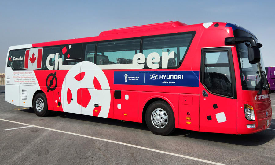 A red and white bus, branded for the FIFA World Cup Qatar 2022, displays 'Canada,' a Canadian flag, 'Cheer!', and a large soccer ball graphic.
