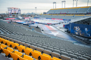 "An outdoor hockey rink is set up in a large stadium with rows of empty seats, featuring ""Heritage Classic"" banners."