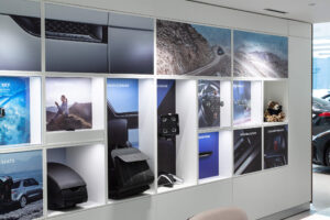A display wall in a car dealership features Jaguar and Land Rover vehicle accessories and lifestyle images across multiple illuminated cubbies and large format posters.
