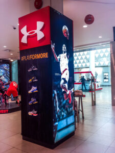 Under Armour retail display column featuring basketball shoes and a digital screen with a basketball player in a store.