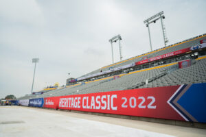 "Empty stadium stands and ground-level perimeter are decorated with ""HERITAGE CLASSIC 2022"" banners under a cloudy sky."